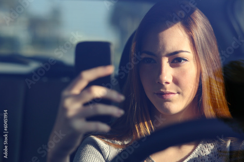 Fotografie, Obraz Front view of a woman driving a car and typing on a smart phone