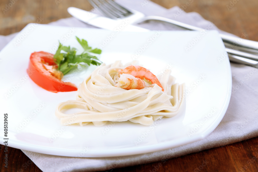 Pasta with shrimps on white plate, on wooden background