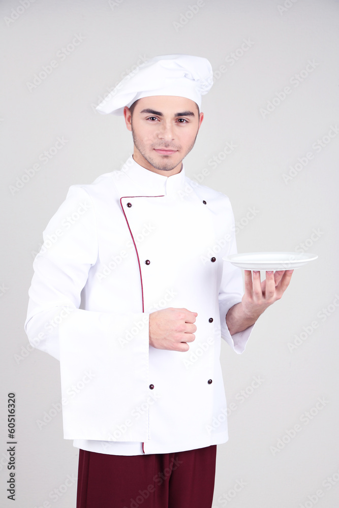 Professional chef in white uniform and hat, on gray background
