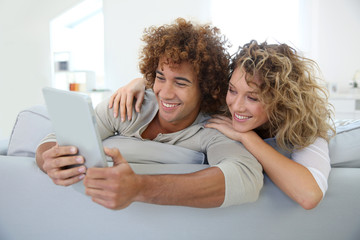 Wall Mural - Cheerful couple having fun using tablet in sofa