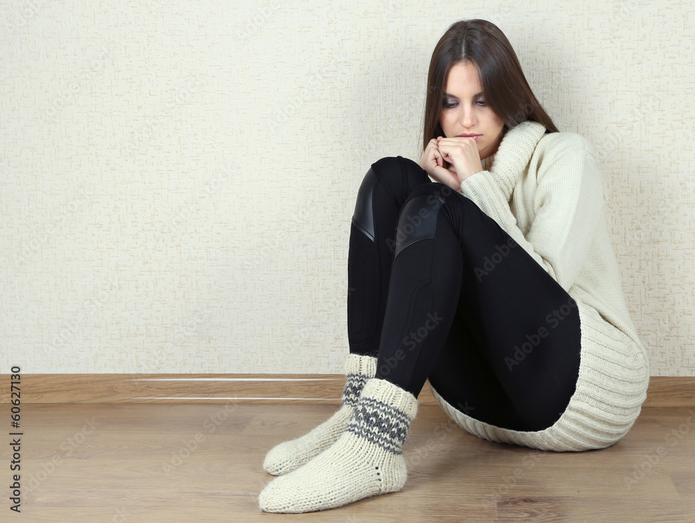Sad woman sitting on floor near wall