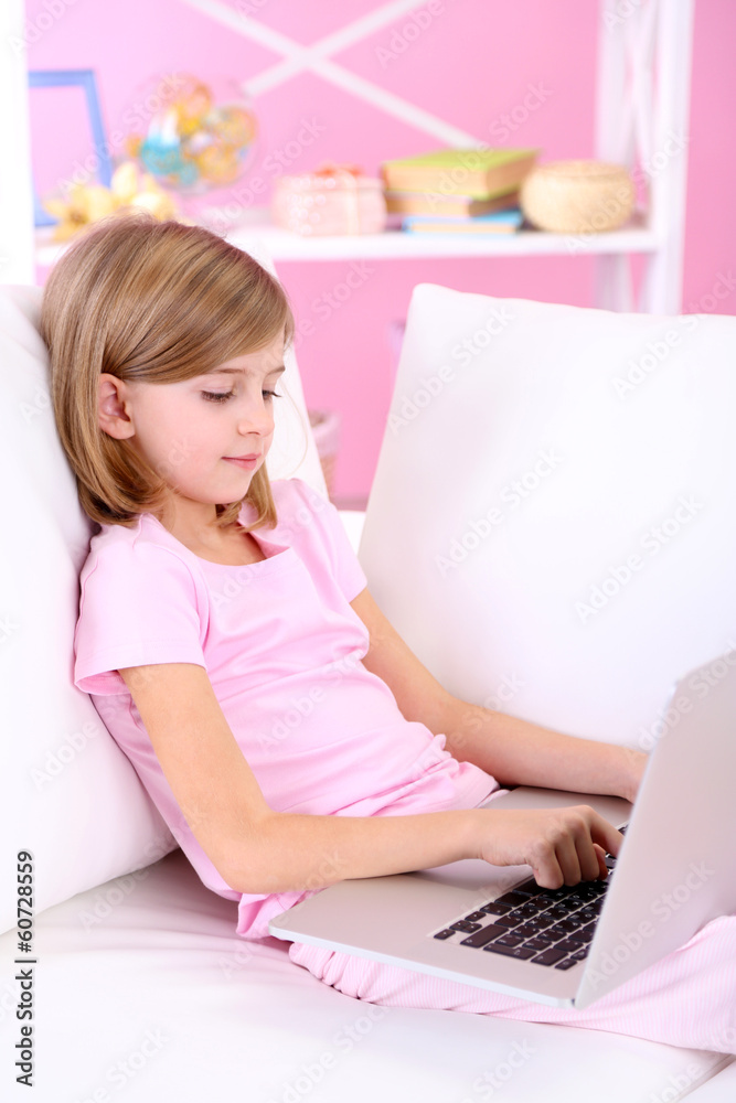 Little girl sitting with laptop on sofa in room