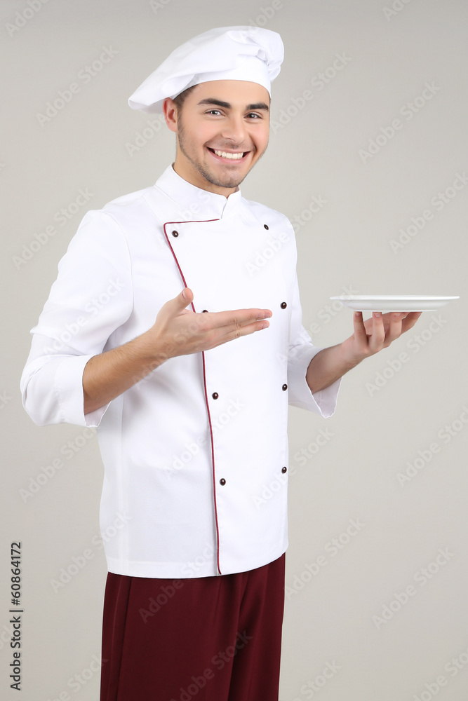 Professional chef in white uniform and hat, on gray background