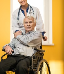 Wall Mural - Cheerful young nurse woman with senior man in wheelchair