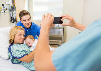 Fototapete - Nurse Photographing Couple With Newborn Baby Through Mobilephone