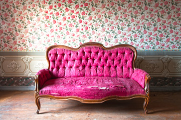 old damaged red couch in an antique house. flowers wallpaper