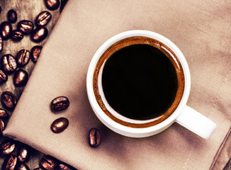 Poster - Cup of coffee with coffee beans on  brown napkin on wooden table