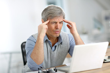 Wall Mural - Senior businessman in front of laptop having a headache