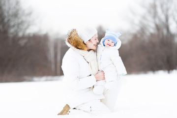 Wall Mural - Young attractive woman playing with her baby in a snowy park