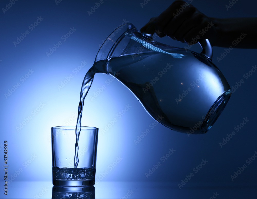 Pour water from  pitcher into  glass, on dark blue background