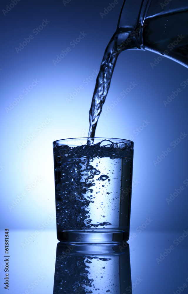 Pour water from  pitcher into  glass, on dark blue background