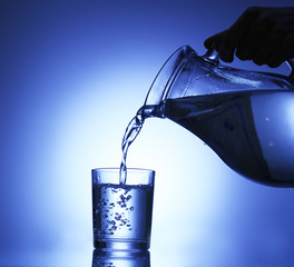 Wall Mural - Pour water from  pitcher into  glass, on dark blue background