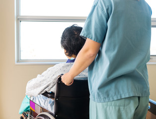 Wall Mural - Patient Sitting On Wheelchair While Nurse Assisting Him At Windo