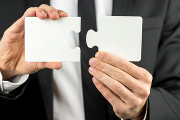 businessman holding two pieces of a blank puzzle