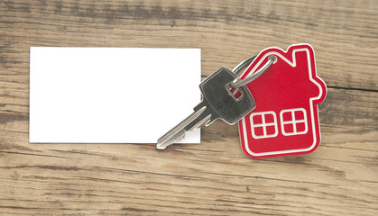 Key with house icon and blank paper on wooden background