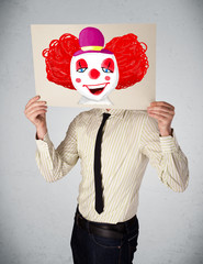 Wall Mural - Businessman holding a cardboard with a clown on it in front of h