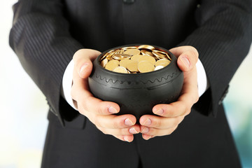 Poster - Ceramic pot with golden coins in male hands, on light