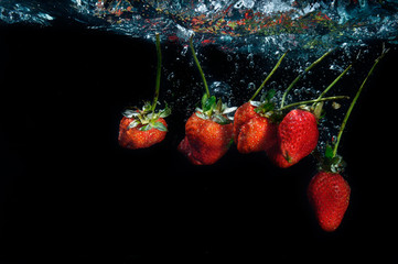 fresh strawberry dropped into water with splash on black backgro