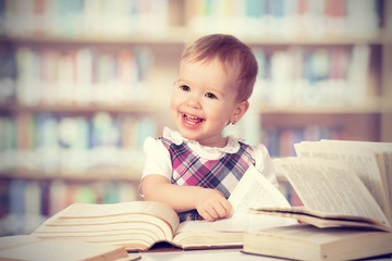 Wall Mural - Happy baby girl reading a book in a library