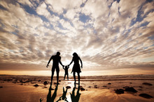 Happy Family Together Hand In Hand On The Beach At Sunset.