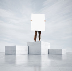 Man standing on a highest cube and holding blank poster