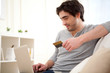 Young relaxed man paying online with credit card in sofa