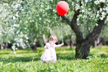 Wall Mural - Funny baby girl walking in an apple tree garden with a red ballo