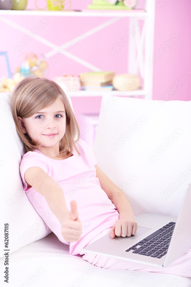 Little girl sitting with laptop on sofa in room