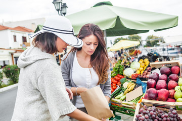 Two women choosing a fruit outdoors in the bio market