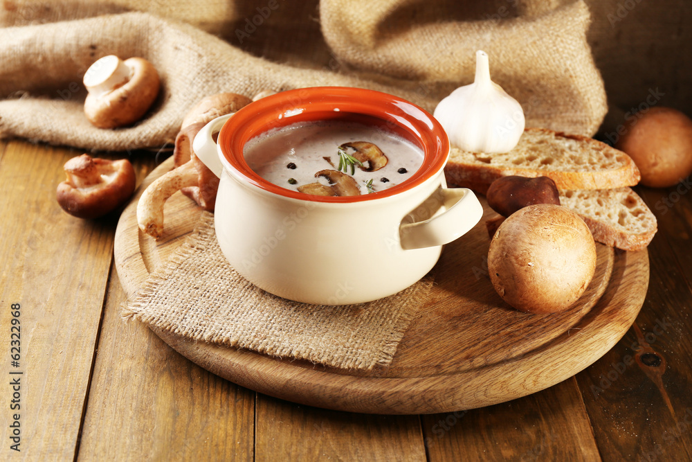 Mushroom soup in pot, on wooden table, on sackcloth background