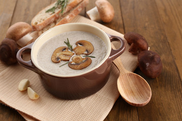 Mushroom soup in pot, on wooden background