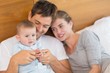 © Wavebreak Media - Happy parents relaxing on bed with their baby son