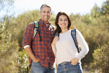 Canvas Print - Portrait Of Couple Hiking In Countryside Wearing Backpacks