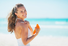 Smiling Young Woman On Beach Applying Sun Block Creme