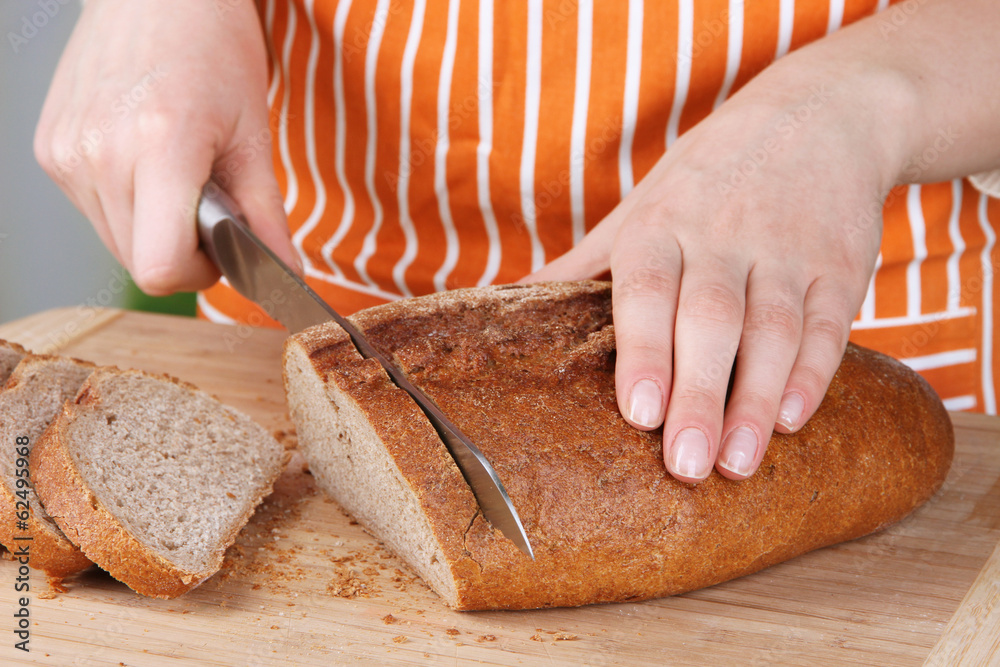 Cutting bread on wooden board on bright background