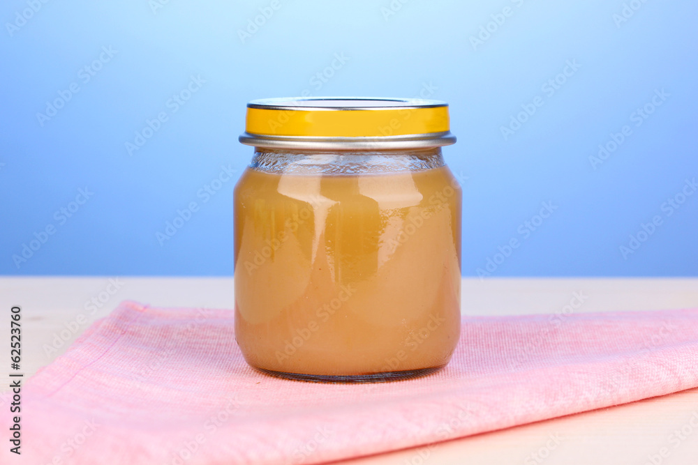 Jar of baby puree on napkin on blue background