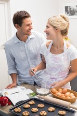 Wall Mural - Happy young couple preparing cookies in kitchen