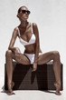 Beautiful tan female model posing in bikini and sunglasses. Agai