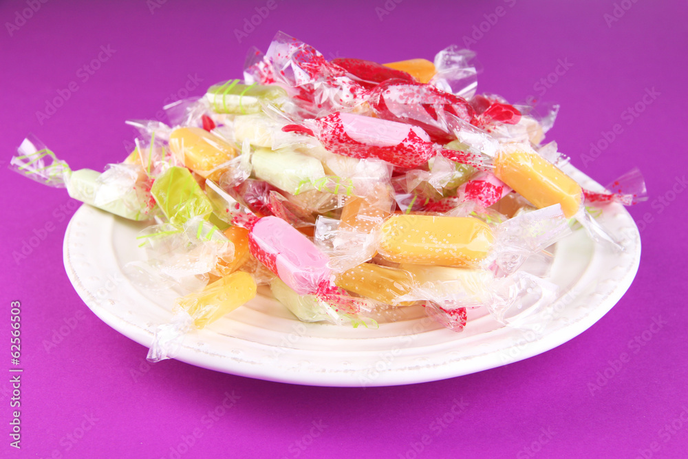 Tasty candies on plate on purple background