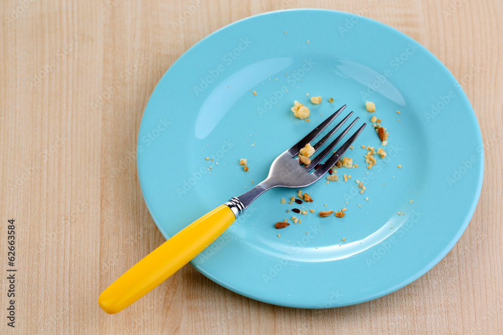 Plate with crumbs and used fork on wooden background