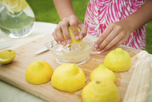 A Summer Family Gathering At A Farm. A Girl Slicing And Juicing Lemons To Make Lemonade.