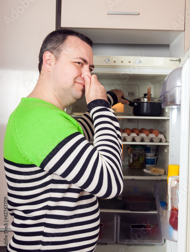 Fotografia, Obraz Guy looking for something in pan near fridge