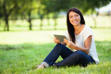 Beautiful Young Woman With Digital Tablet Sitting On Grass In Pa