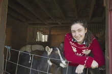 A Goat Farm. A Young Girl Leaning On The Barrier Of The Goat Shed, With A Group Of Goats Behind Her.