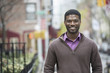 © Mint Images - Outdoors in the city in spring. An urban lifestyle. A young man wearing a purple shirt and jersey smiling.