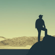 Silhouette Of A Hiker Wearing A Backpack, Pausing To Take In View Of Mountains And Desert In Death Valley National Park.