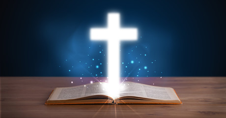 Open holy bible with glowing cross in the middle