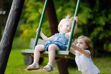 Wall Mural - Two little sisters having fun on a swing