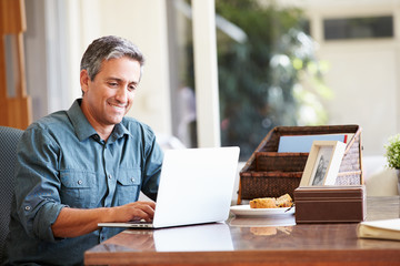 Mature Hispanic Man Using Laptop On Desk At Home