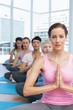 © WavebreakMediaMicro - Class sitting with joined hands in a row at yoga class